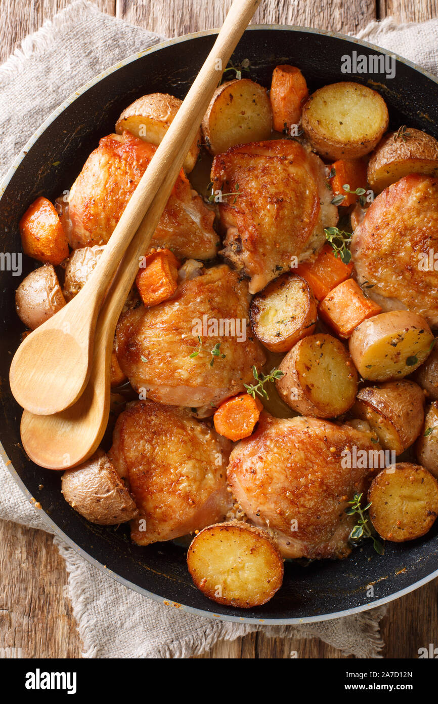 La nourriture française de cuisses de poulet au four avec des pommes de terre, carottes, thym, romarin, sauce épicée close-up dans une casserole sur la table. Haut Vertical Vue de dessus Banque D'Images