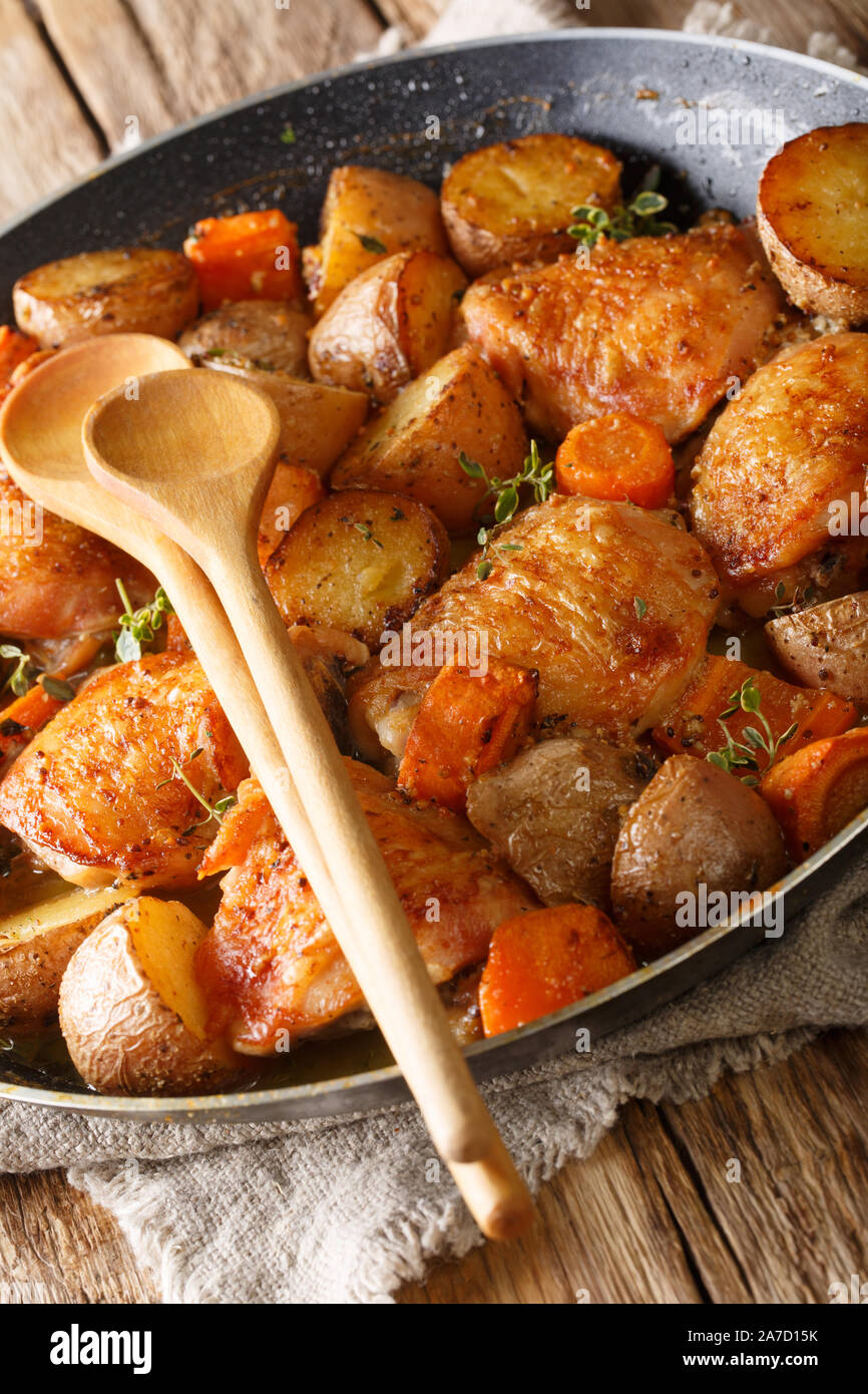 La nourriture française de cuisses de poulet au four avec des pommes de terre, carottes, thym, romarin, sauce épicée close-up dans une casserole sur la table verticale. Banque D'Images