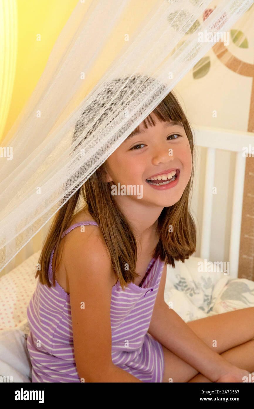Sept ans, fille, assise sur son lit Banque D'Images