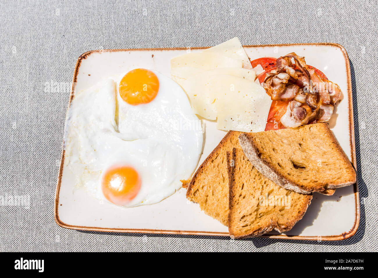 Une assiette de petit-déjeuner avec des œufs, tomate, pain, fromage et bacon, graviera vue supérieure Banque D'Images