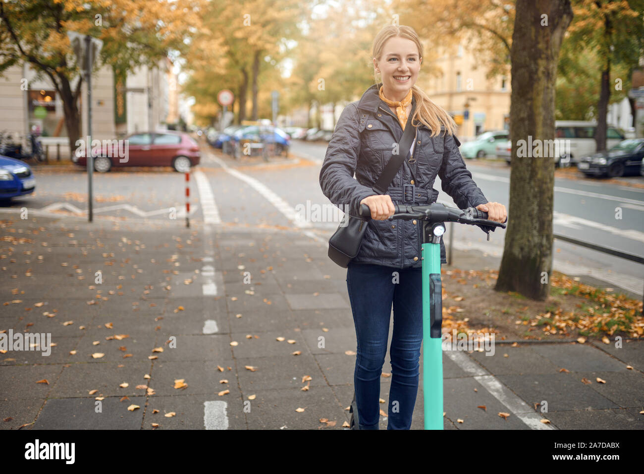Young happy blonde woman riding scooter électrique dans la ville, souriant à la caméra, à l'automne Banque D'Images