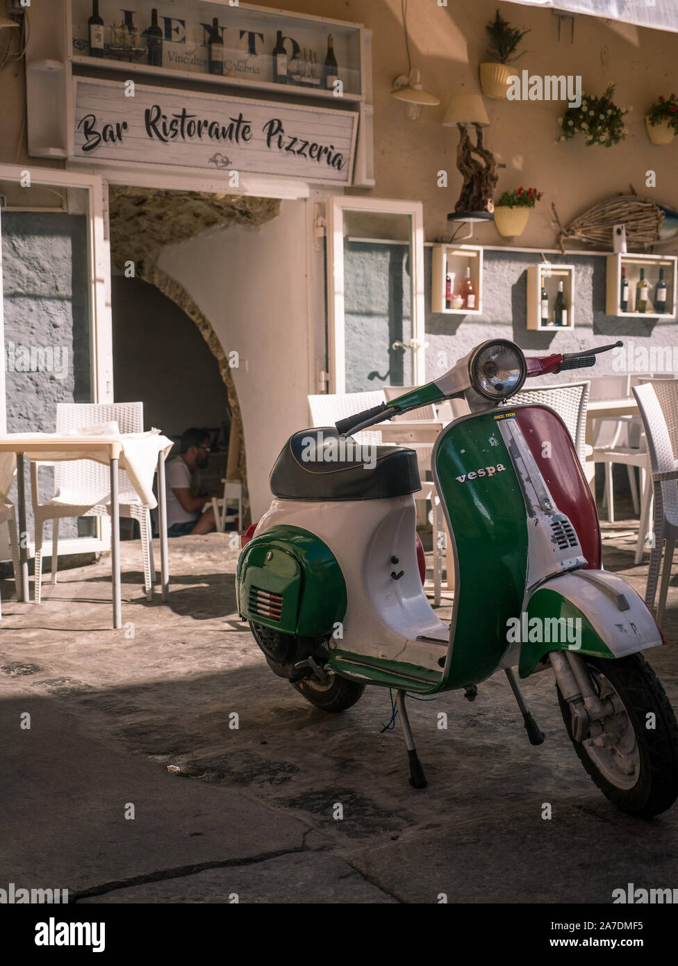 Moto Vespa en couleurs de drapeau italien en face de restaurant traditionnel et pizzeria avec lettrage à Tropea, Calabre, Italie Banque D'Images