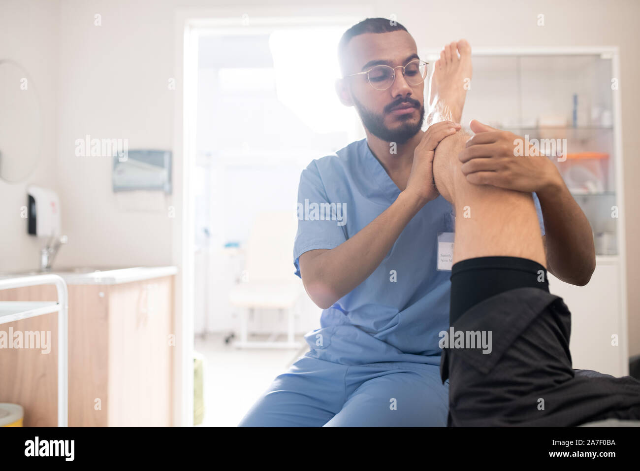 Jeune professionnel du genou du patient de masser tout en tenant sa jambe sur l'épaule Banque D'Images