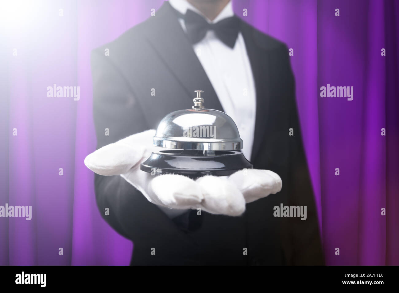 Portrait Waiter Holding Bell Service sur Main contre Rideau pourpre Banque D'Images