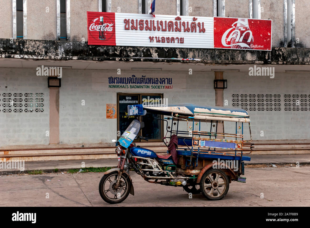 Une Honda tuk tuk avec un logo de marque Pepsi peintes sur le réservoir de gaz est placée sous un des panneaux publicitaires Coca Cola en Nong Khai, Thaïlande du Nord. Banque D'Images