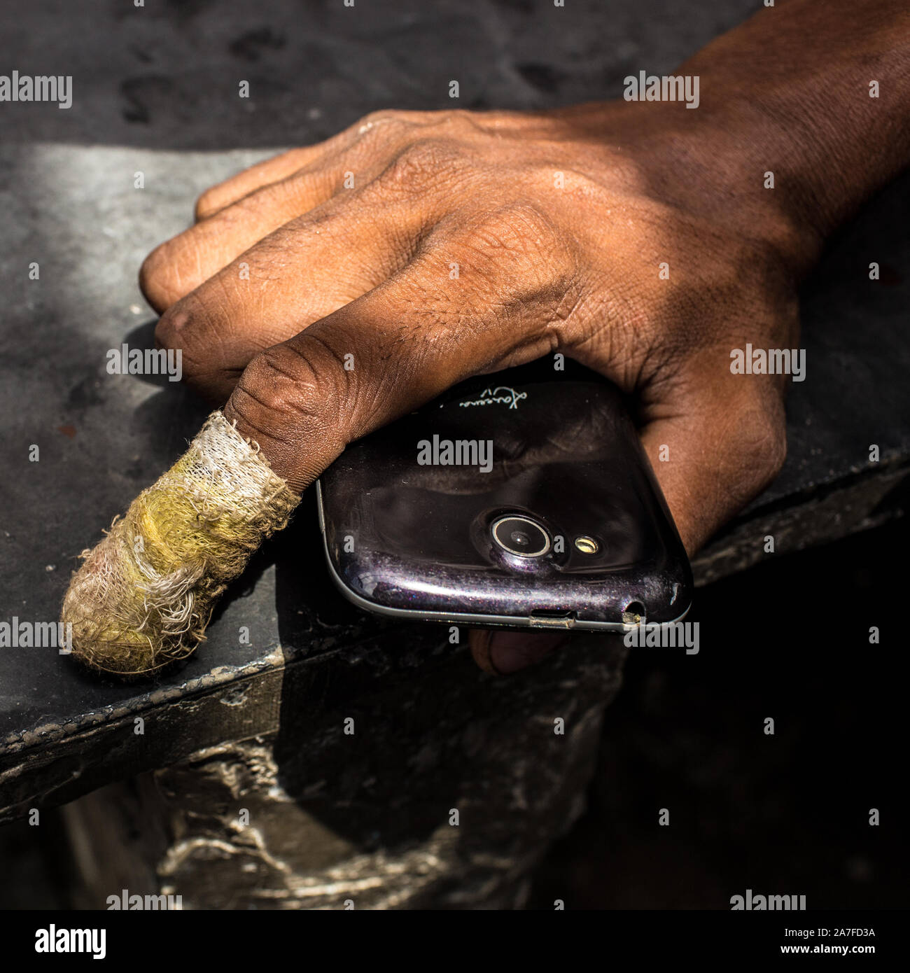 Portrait d'un Indien tenant son téléphone cellulaire avec un doigt bandé qui l'antiseptique s'est infiltré à travers Banque D'Images