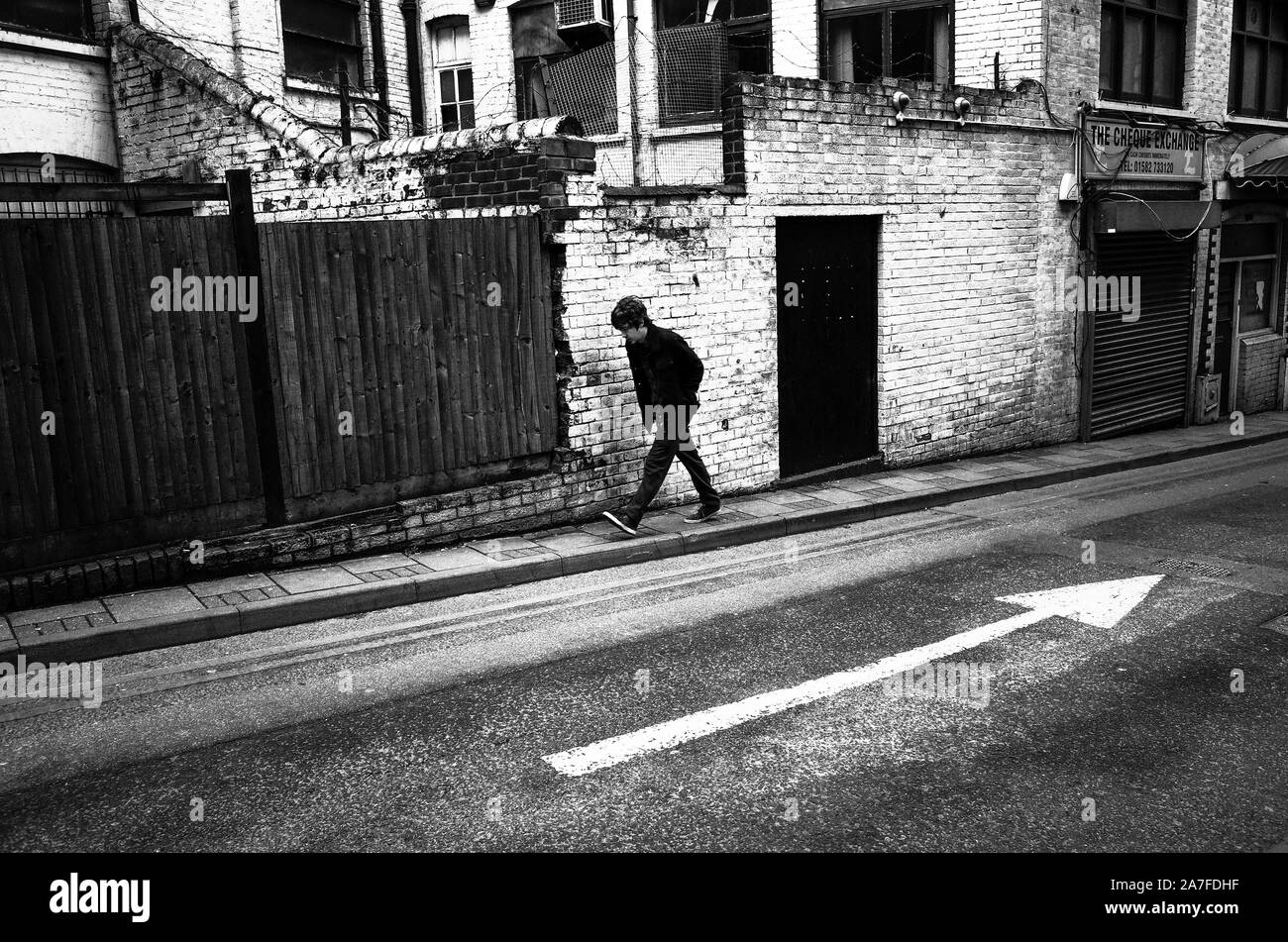 L'homme fait son chemin d'une route en pente dans le sens inverse de la flèche d'une route pour faire une composition intéressante Banque D'Images