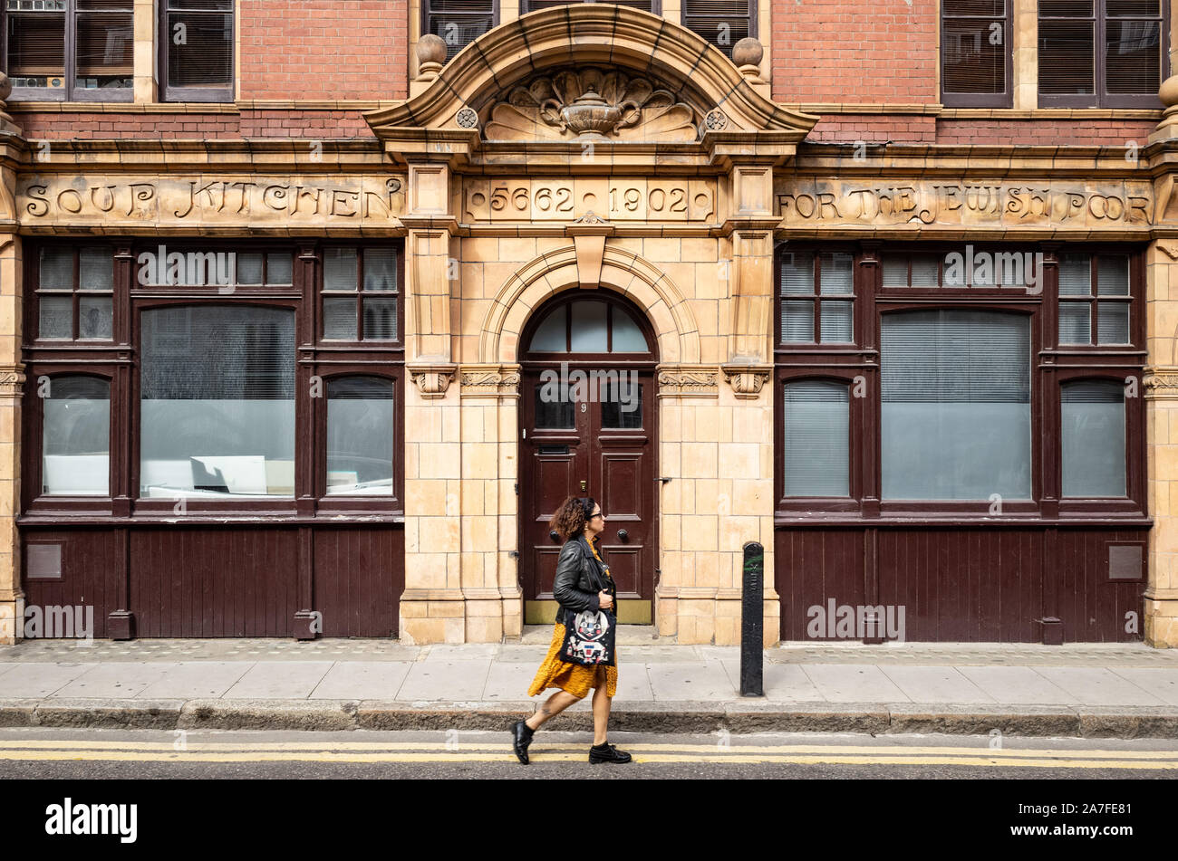Une dame marche dernières bâtiment construit en 1902. Au-dessus de la porte enregistre son but original était une soupe populaire pour les pauvres juifs vivant dans l'Est de Londres, UK Banque D'Images