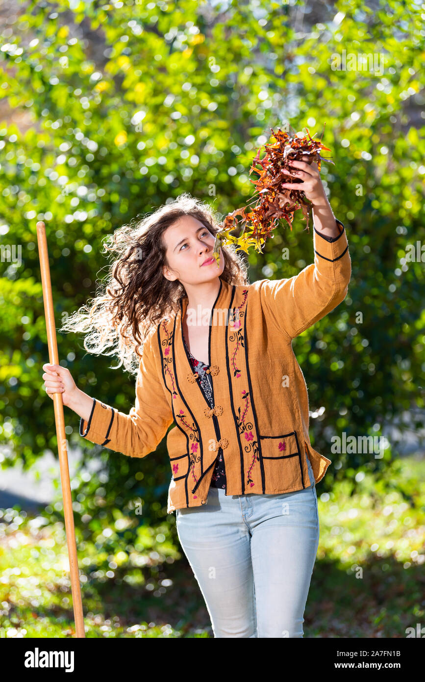 Jeune femme propriétaire d'une arrière-cour de triage dans la collecte de ratisser les feuilles de chêne sec feuillage d'automne feuillage holding permanent avec le râteau dans l'automne ensoleillé Banque D'Images