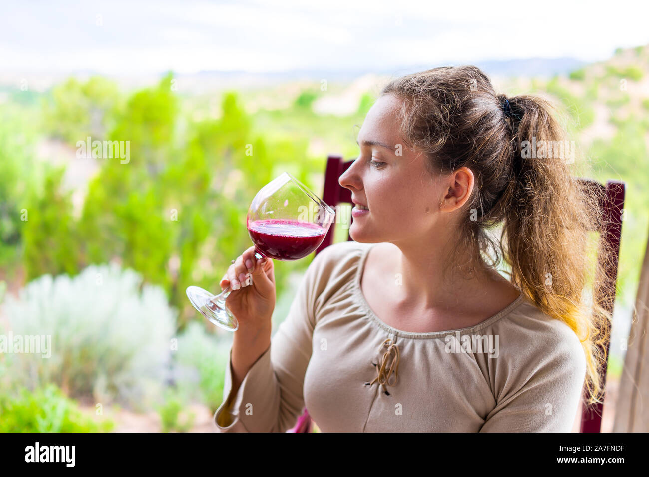 Happy woman assis dehors dans un fauteuil à bascule de boire dans un verre de vin rouge rose vert violet ou le jus de canneberge à Santa Fe backyard jardin désert Banque D'Images