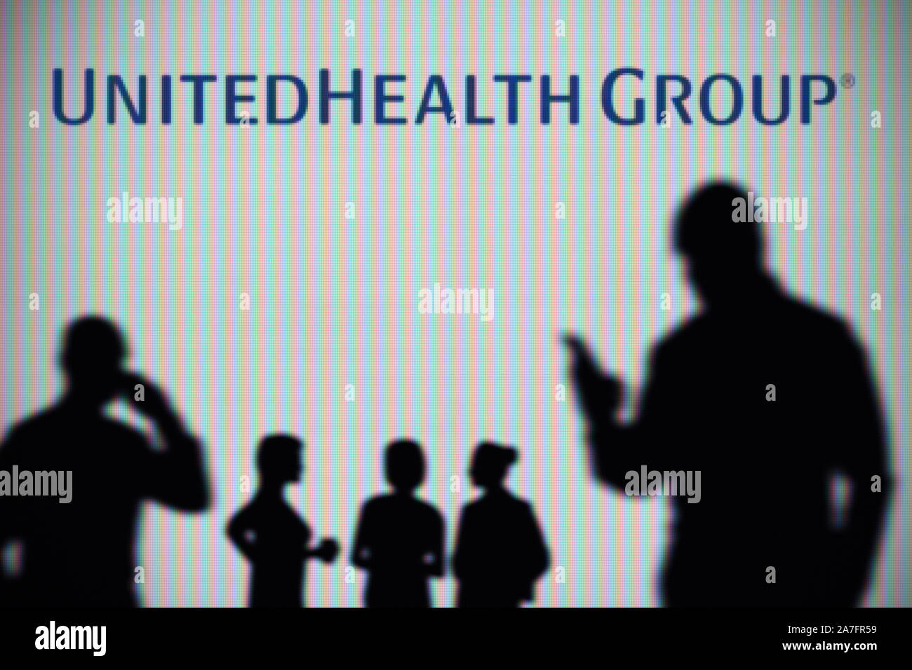 L'UnitedHealth Group logo est visible sur un écran LED à l'arrière-plan tandis qu'une silhouette personne utilise un smartphone (usage éditorial uniquement) Banque D'Images