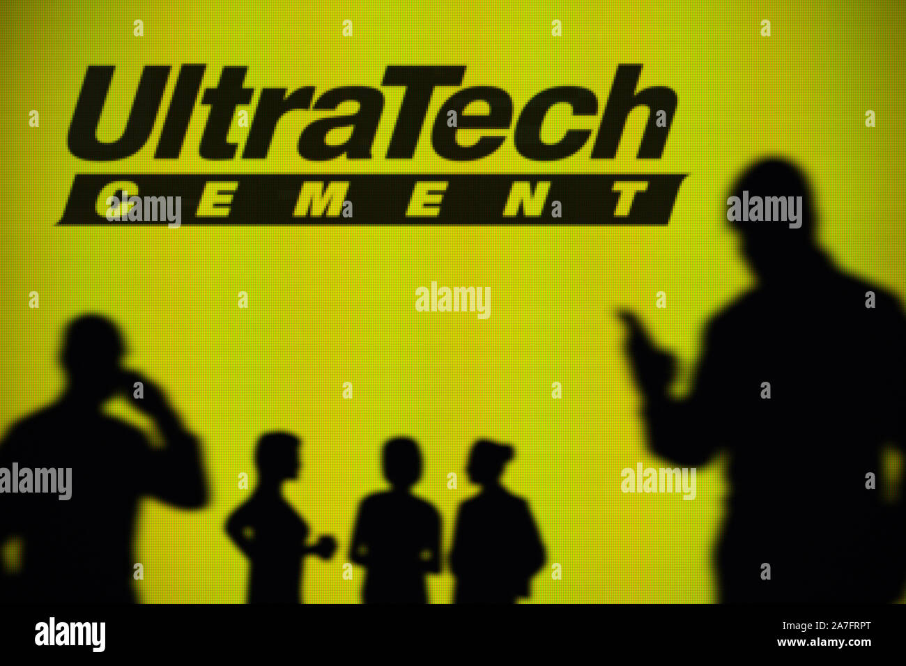 L'UltraTech Cement logo est visible sur un écran LED à l'arrière-plan tandis qu'une silhouette personne utilise un smartphone (usage éditorial uniquement) Banque D'Images