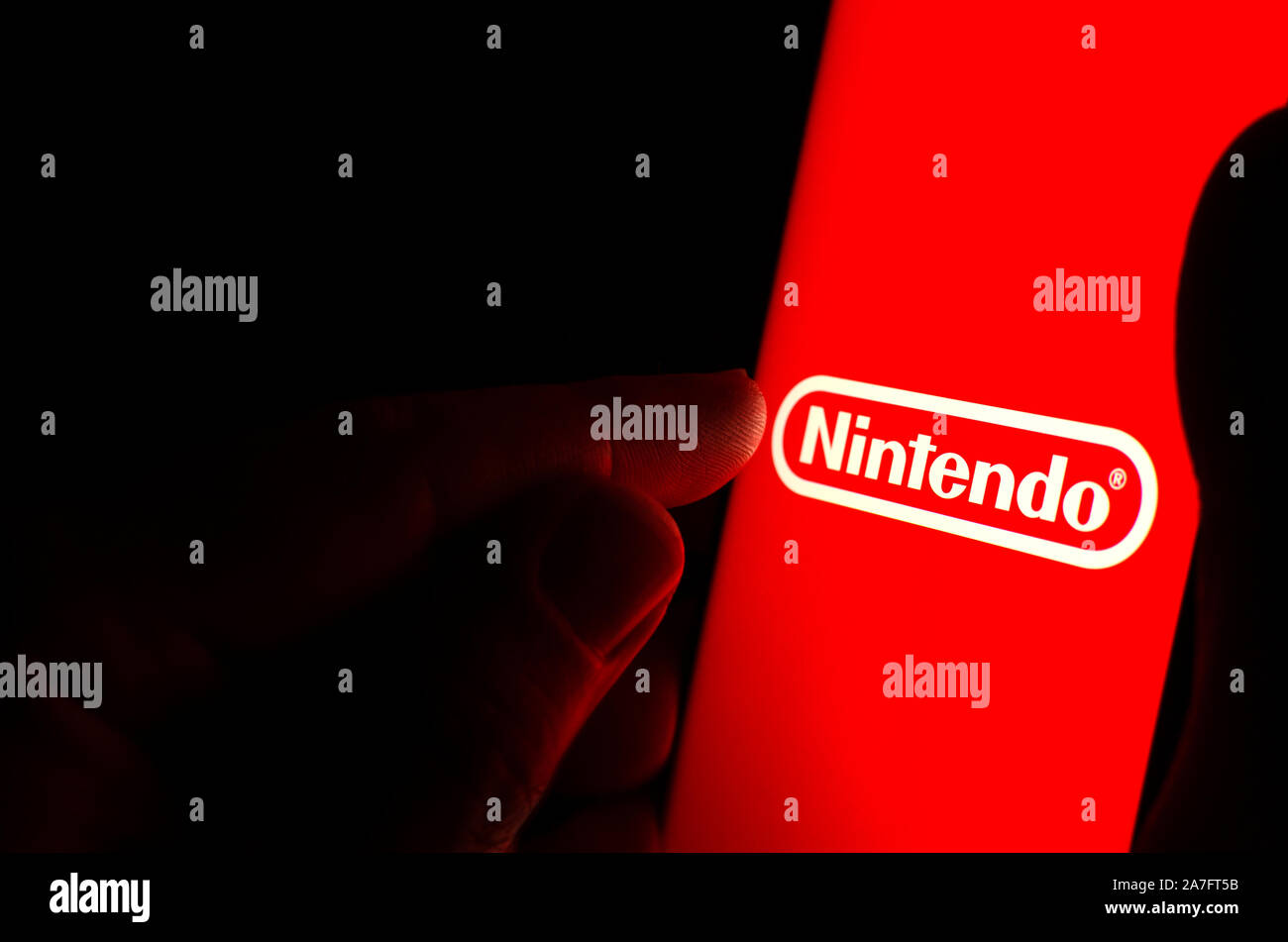 Logo Nintendo sur un écran de smartphone rouge dans une pièce sombre et un doigt de le toucher. Banque D'Images