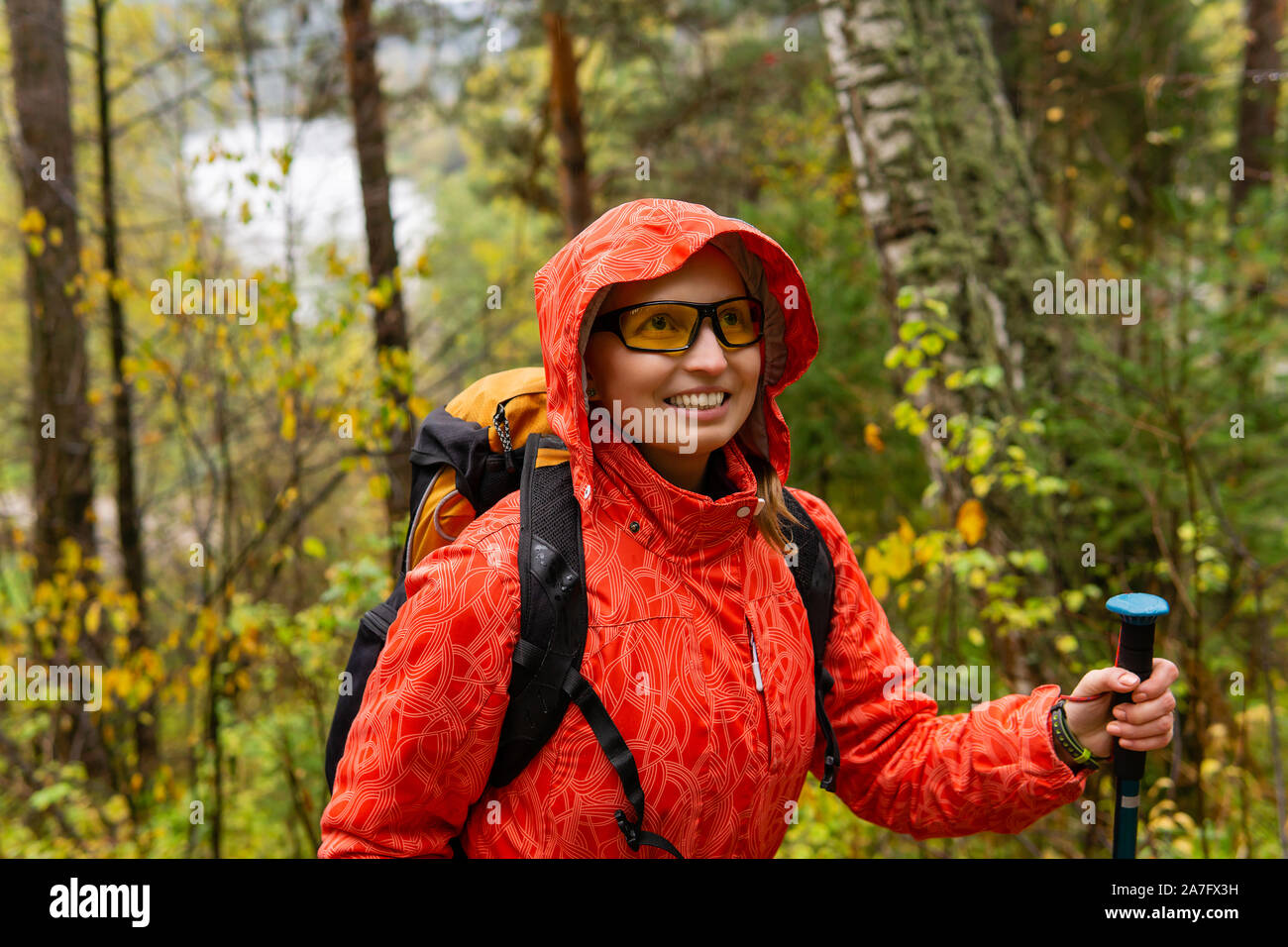 Smiling woman traveler avec un sac à dos de promenades à travers la forêt d'automne par temps de pluie Banque D'Images