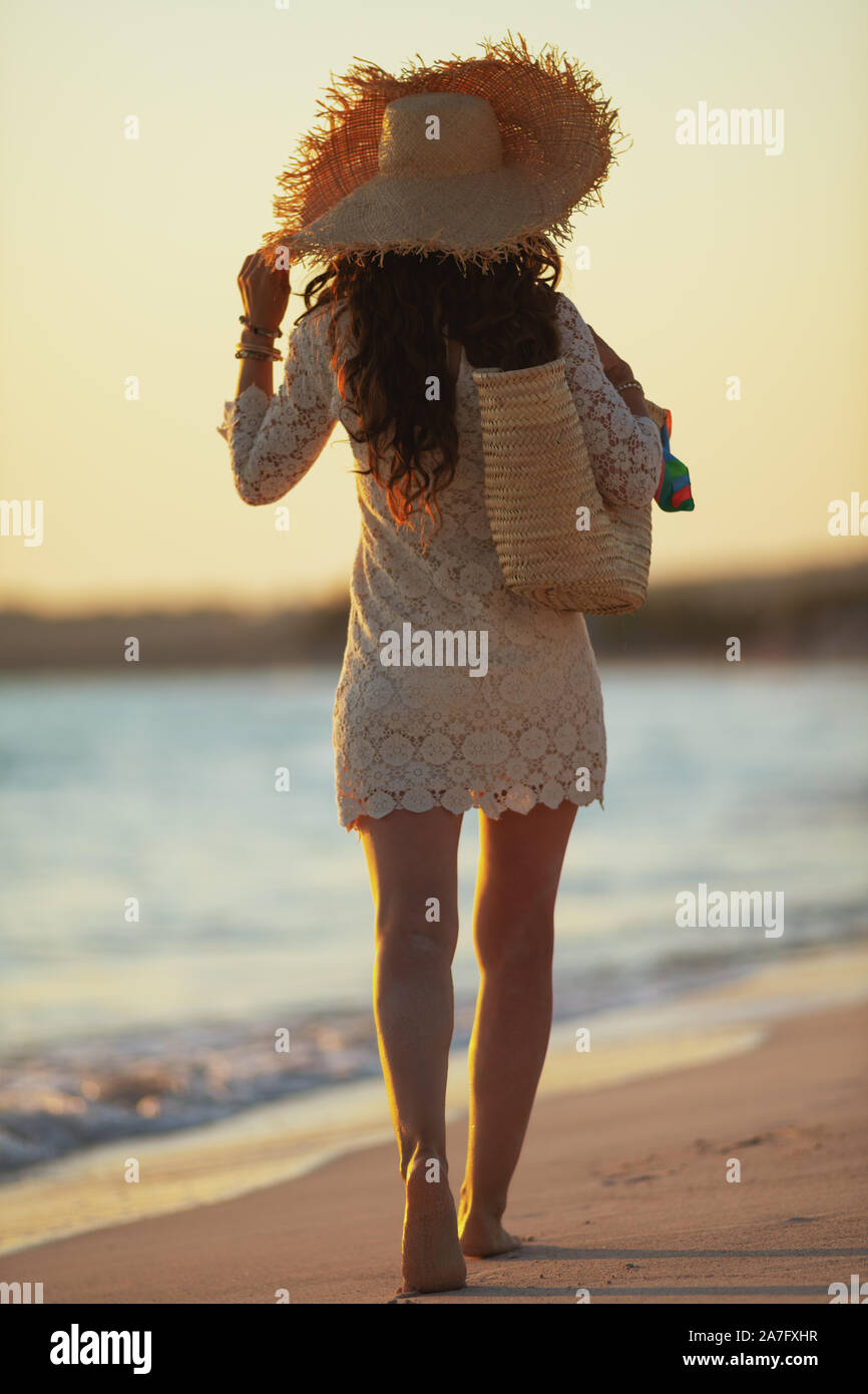 Portrait de jeune femme en robe blanche et chapeau de paille sur le bord de mer au coucher du soleil la marche. Banque D'Images