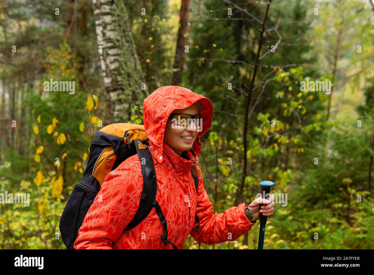 Smiling woman traveler avec un sac à dos de promenades à travers la forêt d'automne par temps de pluie Banque D'Images