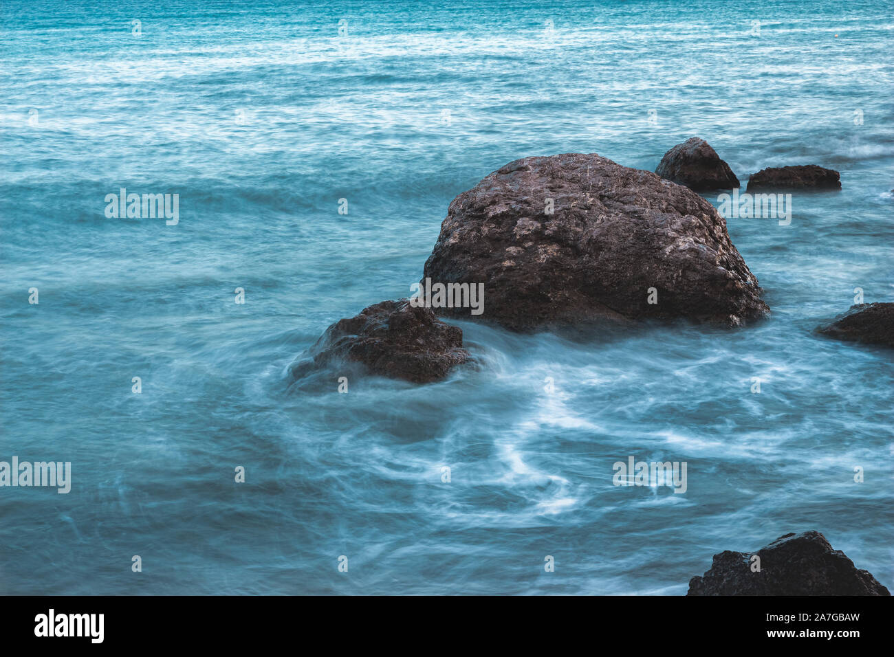 Marin avec des pierres dans l'eau et des vagues à longue exposition. Banque D'Images