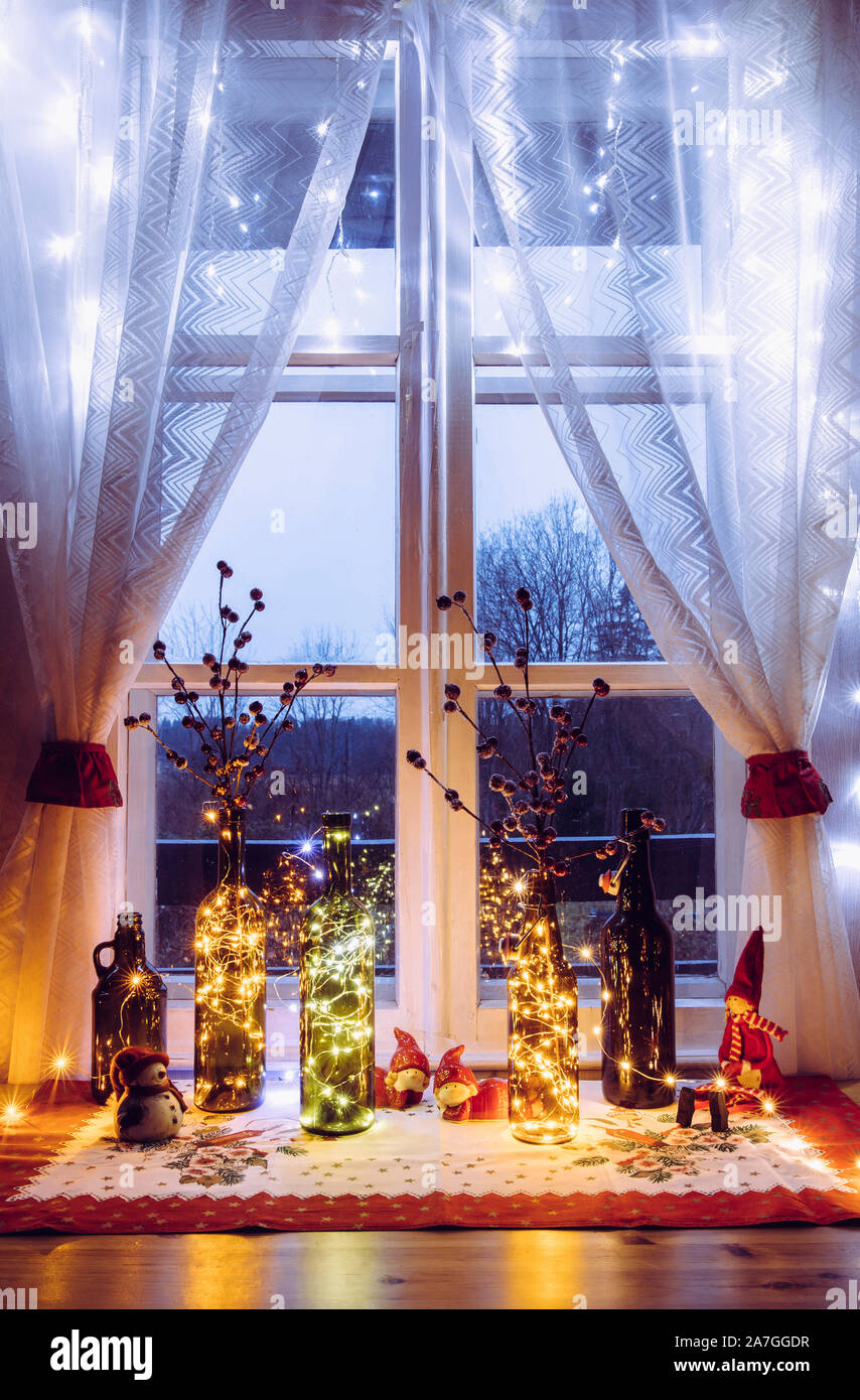 Douillettes et set de décoration de Noël avec des bouteilles de bière et de vin vintage des bouteilles remplies avec led feux micro parti, derrière la fenêtre est campagne Banque D'Images