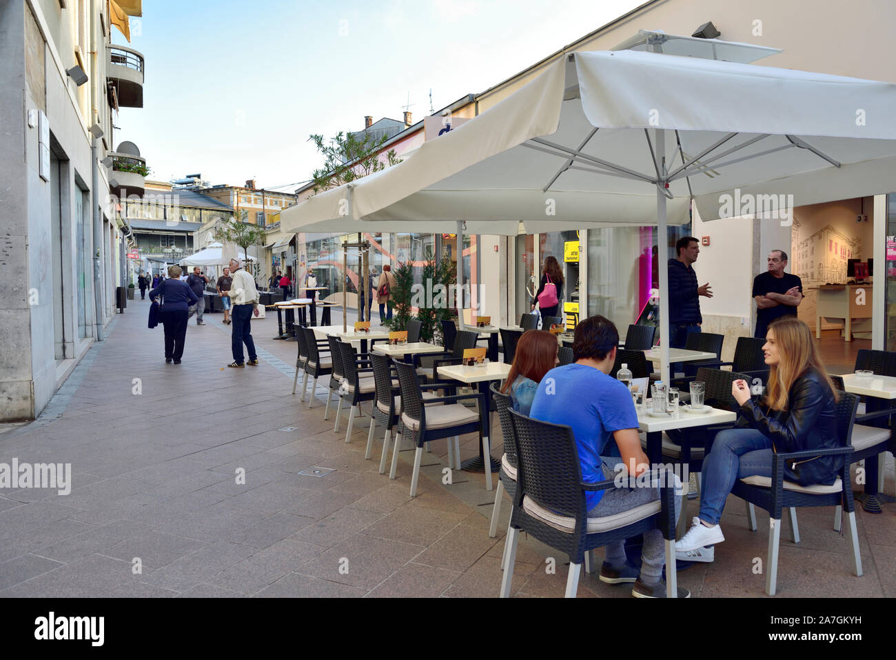 Café avec parapluie à l'extérieur couverts tables, chaises et les gens manger à l'extérieur du trottoir, Banque D'Images