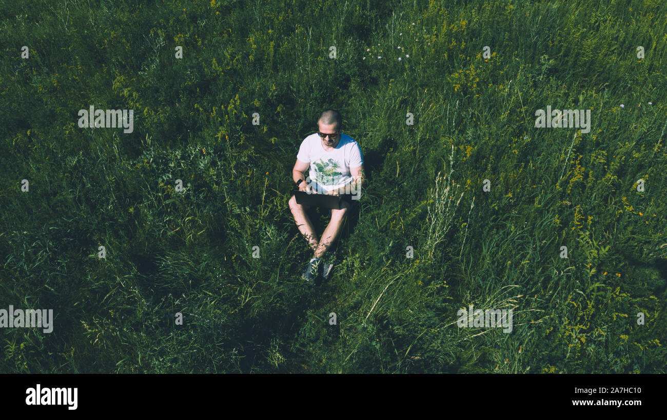 Vue supérieure de la photo aérienne de l'homme assis sur l'herbe avec portable Banque D'Images