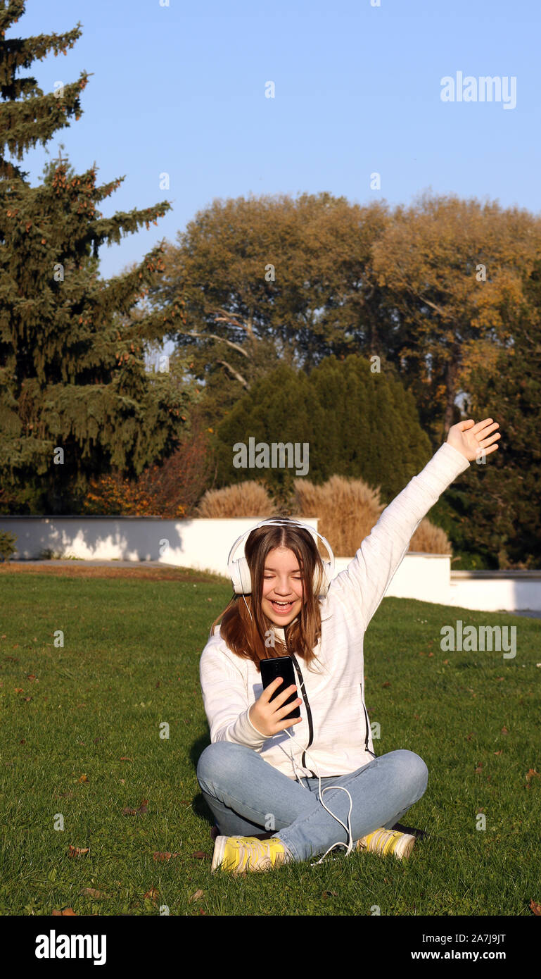 Teenage girl est à l'écoute de la musique à partir de son smartphone in park Banque D'Images