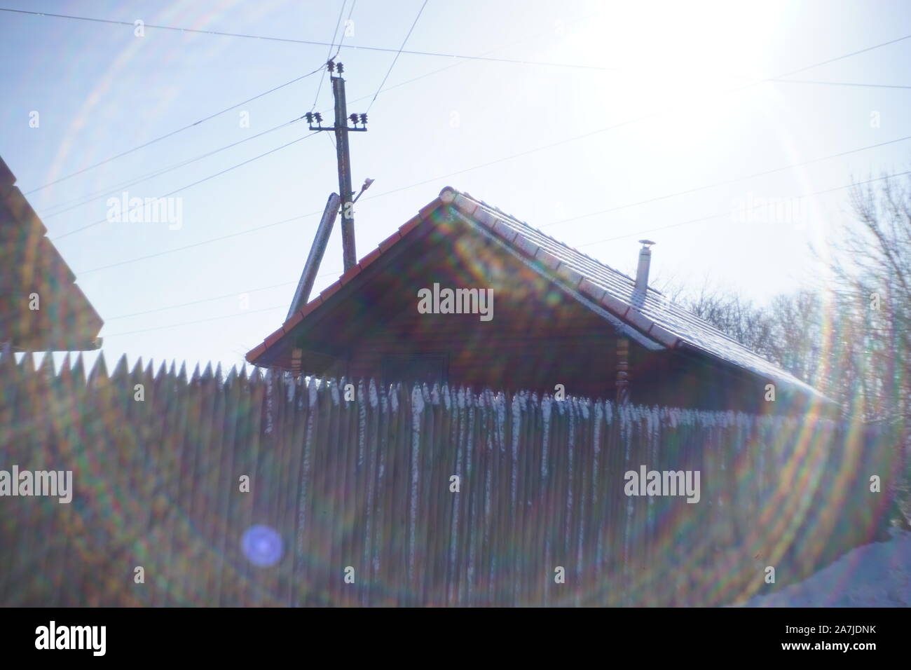 Maison en bois avec une clôture et poteau électrique. Journée ensoleillée d'hiver. Beaux rayons autour. Banque D'Images