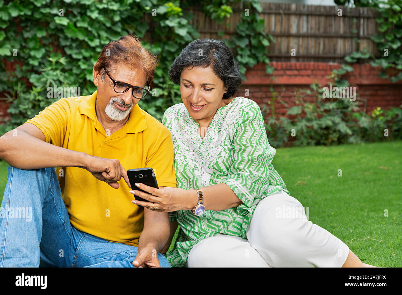 Vieux couple heureux de vous détendre dans le parc et la lecture d'un message texte sur leur téléphone mobile Banque D'Images