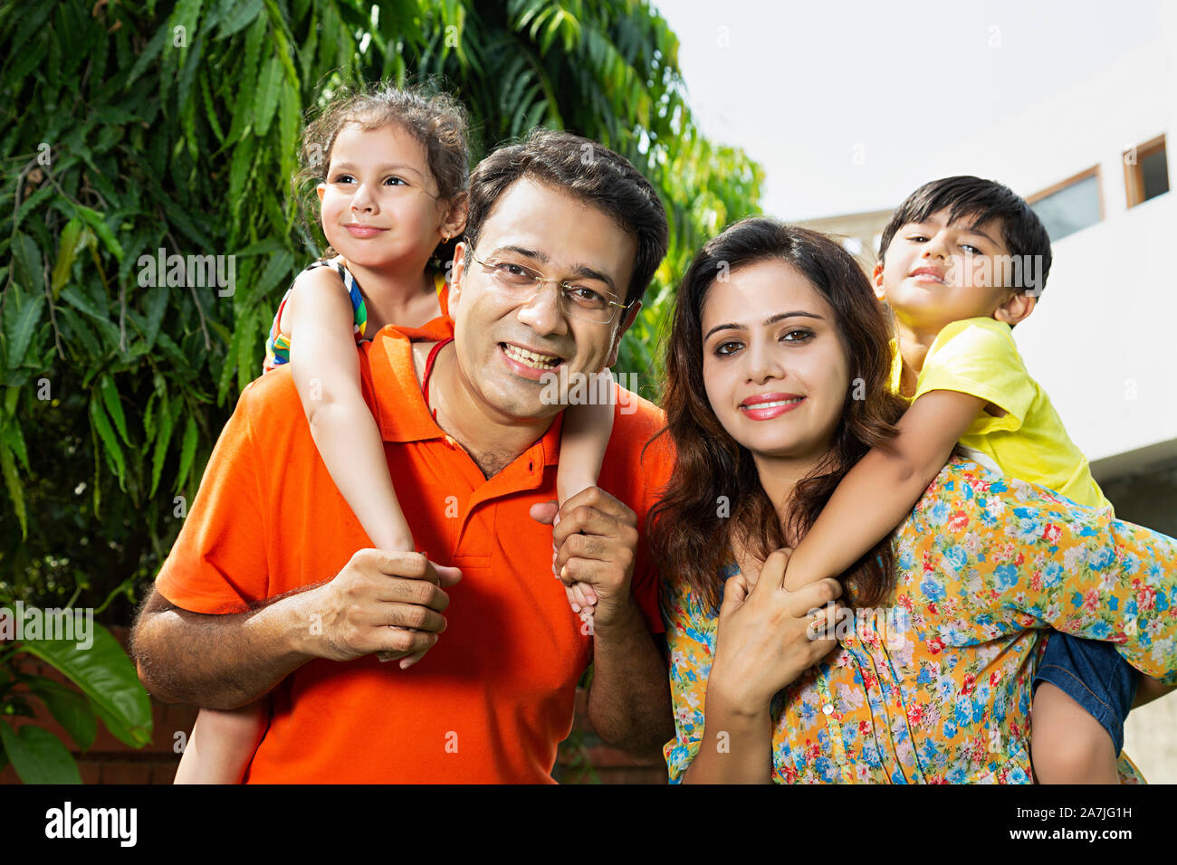 Jeune famille indienne heureux les parents qui piggyback ride to kids en-cour de leur maison à Banque D'Images