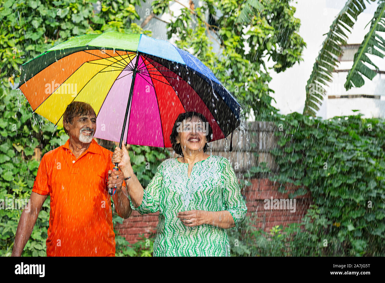Happy Senior couple standing sous la pluie avec un parapluie s'amuser Profitez-en temps de pluie parc Banque D'Images