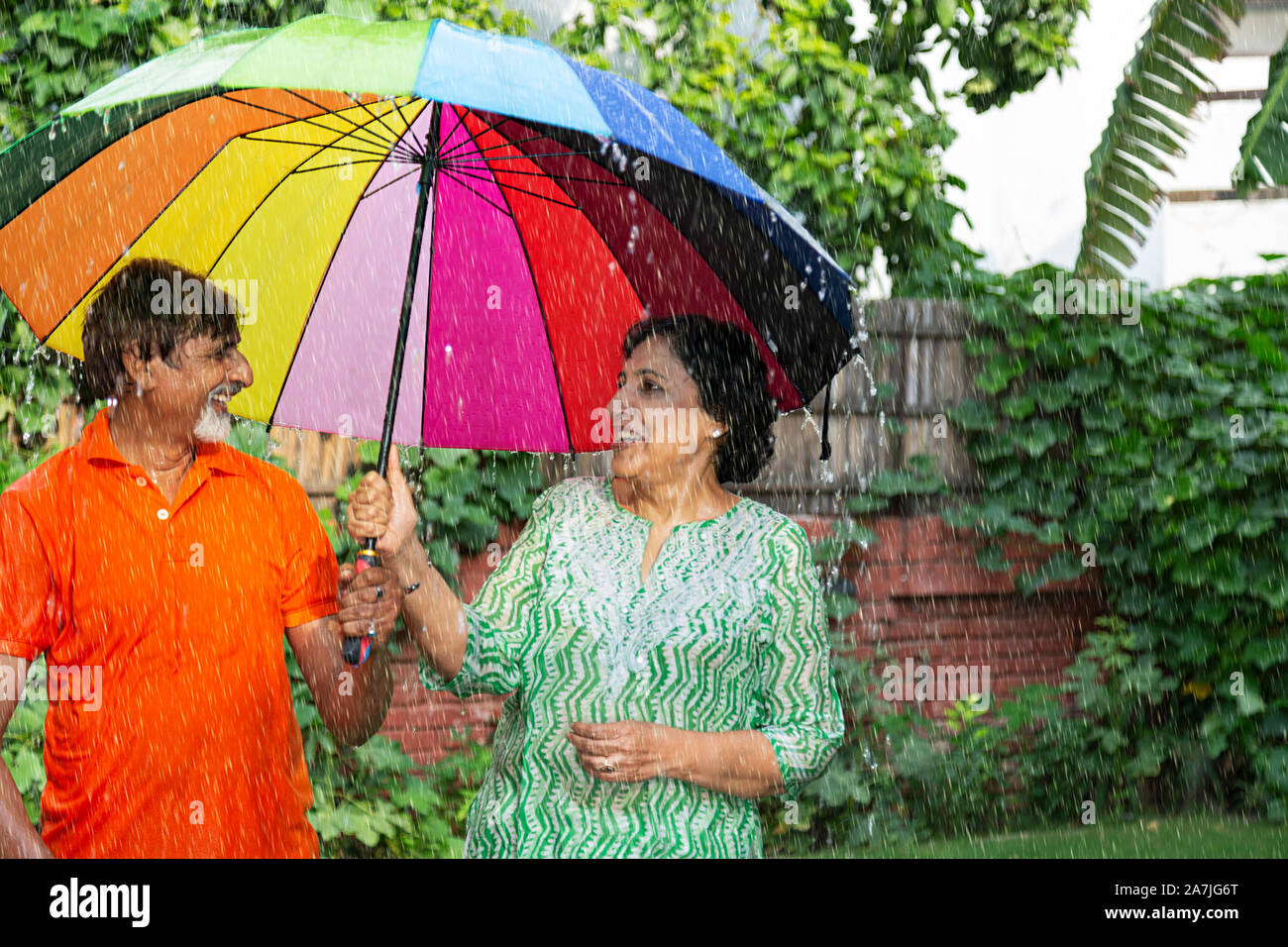 Happy Senior Couple avec parapluie sous la pluie s'amusant dans le jardin Banque D'Images