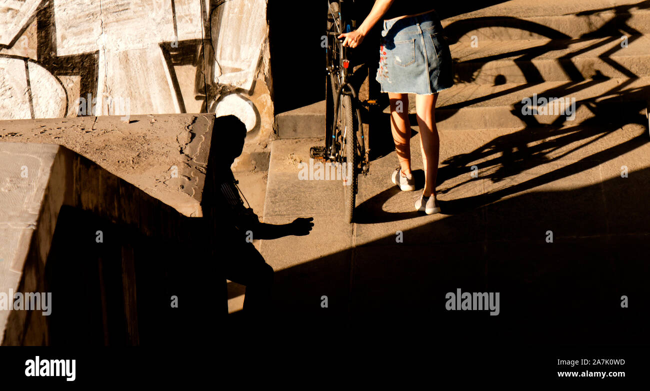 Une adolescente en jupe courte poussant le vélo l'Escalier publics dans la lumière du soleil et les ombres, de derrière Banque D'Images