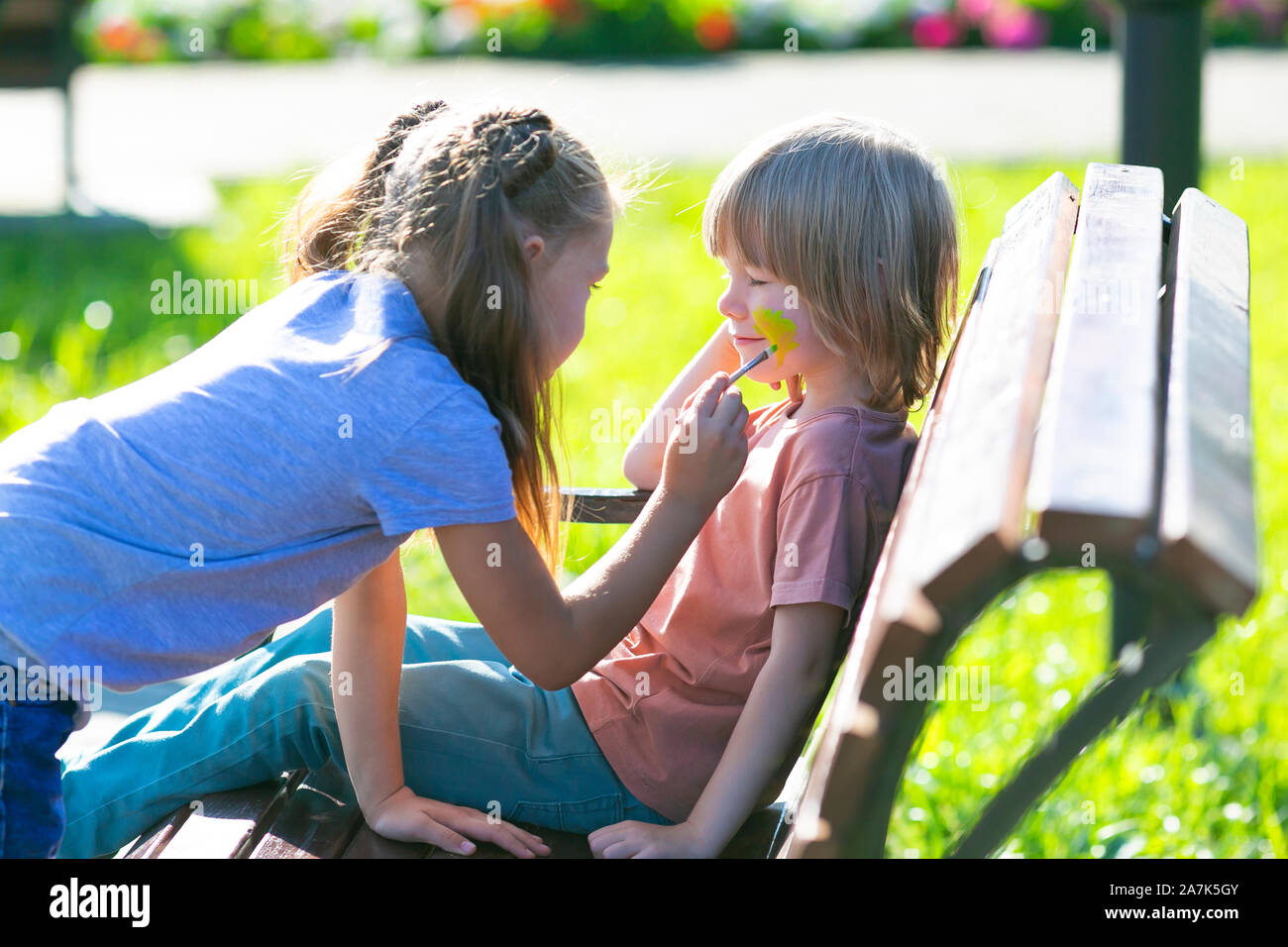 Une petite fille est l'application de maquillage aqua le visage du garçon  de 5 ans qui est assise sur un banc dans un parc Photo Stock - Alamy