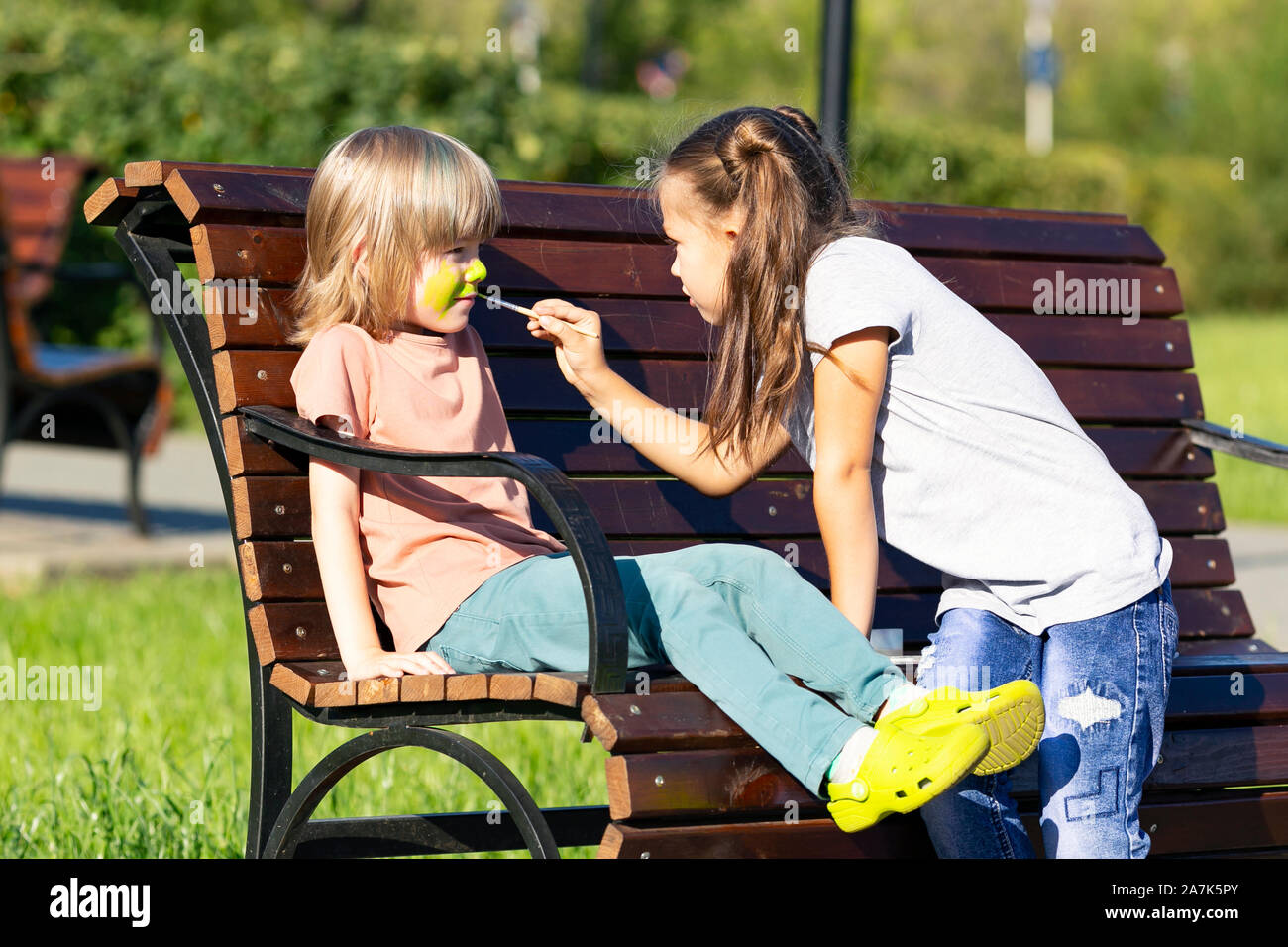 Une petite fille est l'application de maquillage aqua à la face d'un garçon  de 5 ans qui est assise sur un banc de parc Photo Stock - Alamy