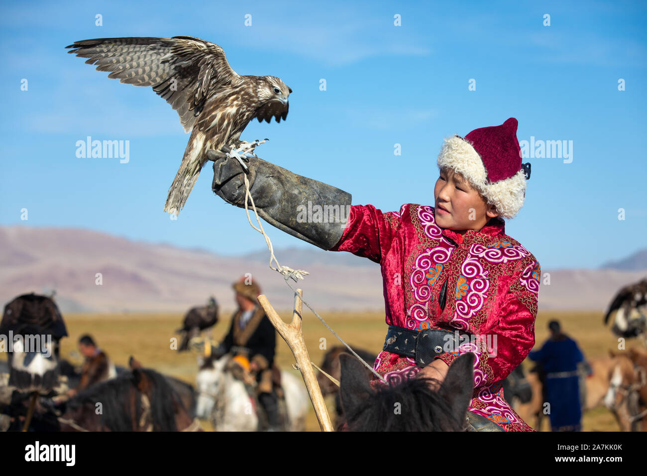 Jeune garçon mongol mongol traditionnel en tenant sa robe de pèlerin à cheval. Les jeunes enfants commencent l'entraînement avec les faucons avant de travailler avec g Banque D'Images
