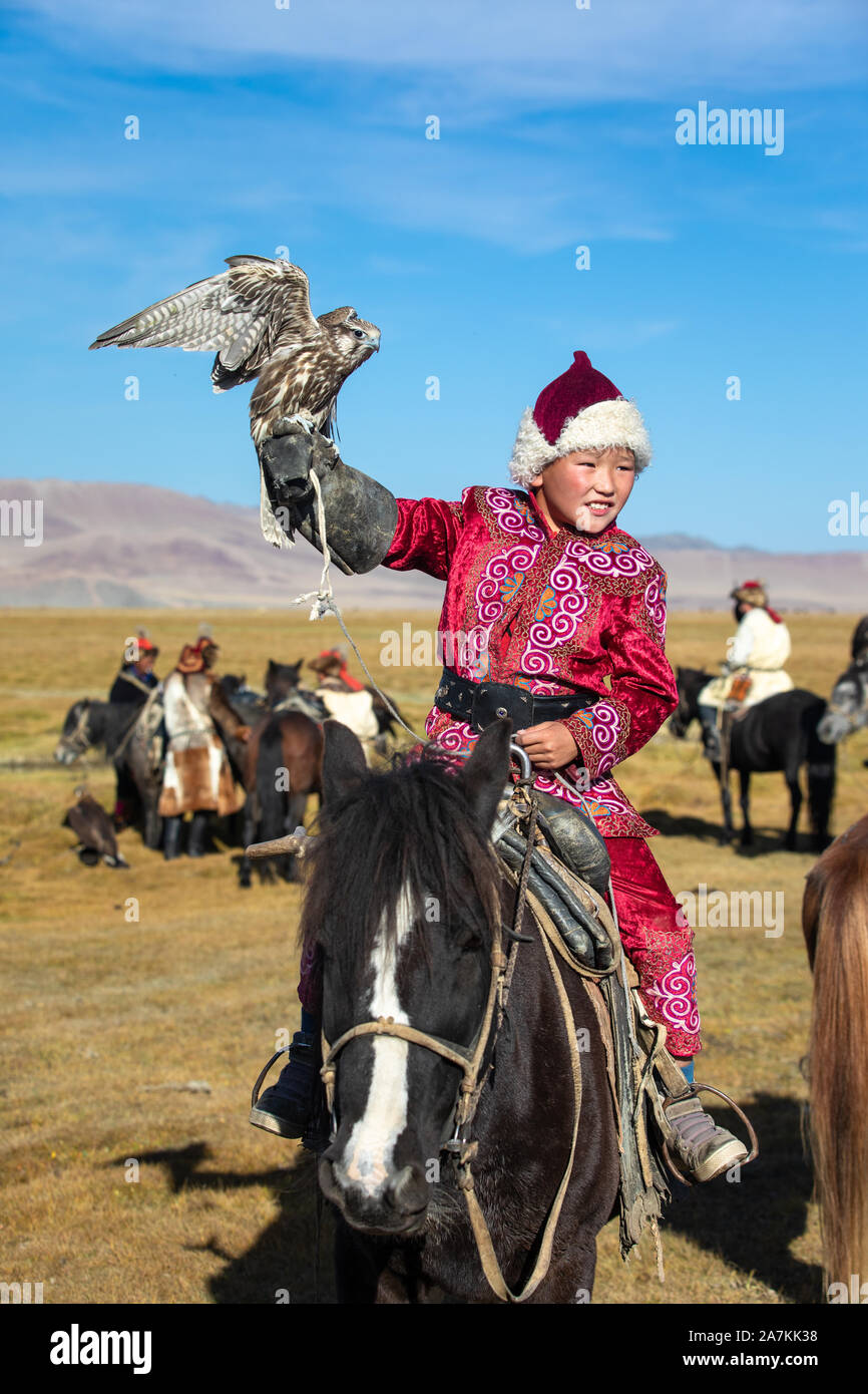 Jeune garçon mongol mongol traditionnel en tenant sa robe de pèlerin à cheval. Les jeunes enfants commencent l'entraînement avec les faucons avant de travailler avec g Banque D'Images