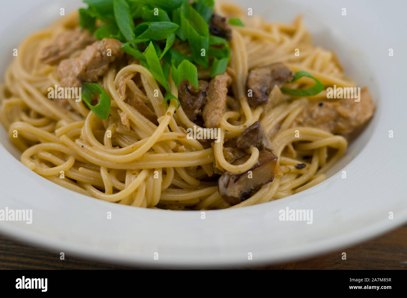 Spaghetti crémeux au poulet et champignons mixtes. Parsemé d'oignons de printemps coupés en rondelles. Fraîchement préparés et servis comme un repas rapide et sain Banque D'Images