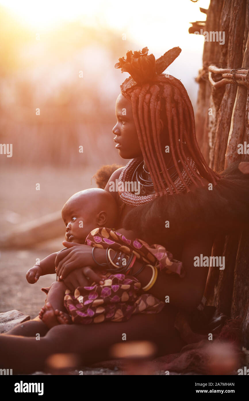 Une jeune femme Himba tenant son bébé à l'extérieur de sa hutte, près des chutes d'Epupa, Namibie. Banque D'Images