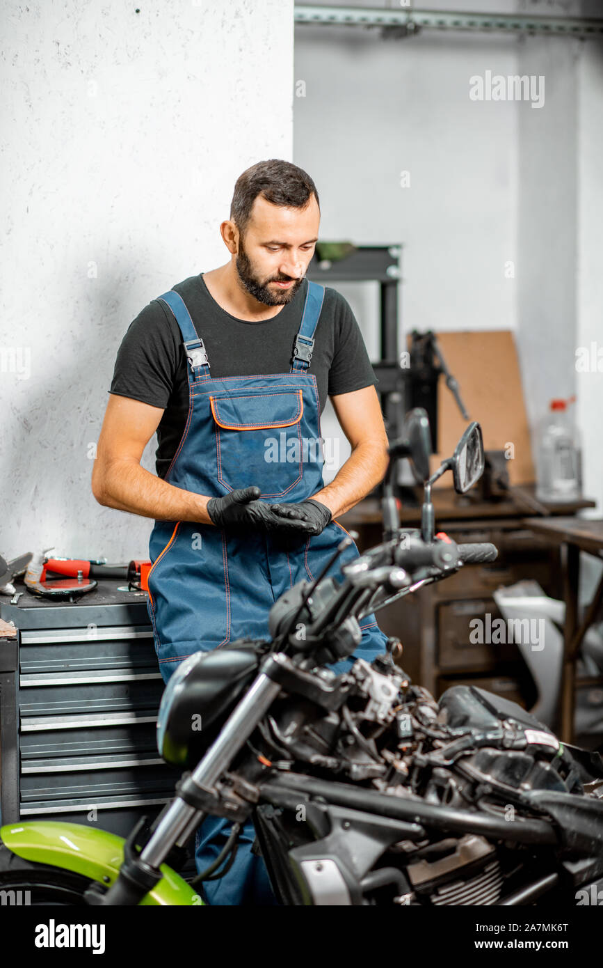 Portrait d'un motard ou réparateur à bretelles de travail debout près de la  moto pendant la réparation dans l'atelier Photo Stock - Alamy