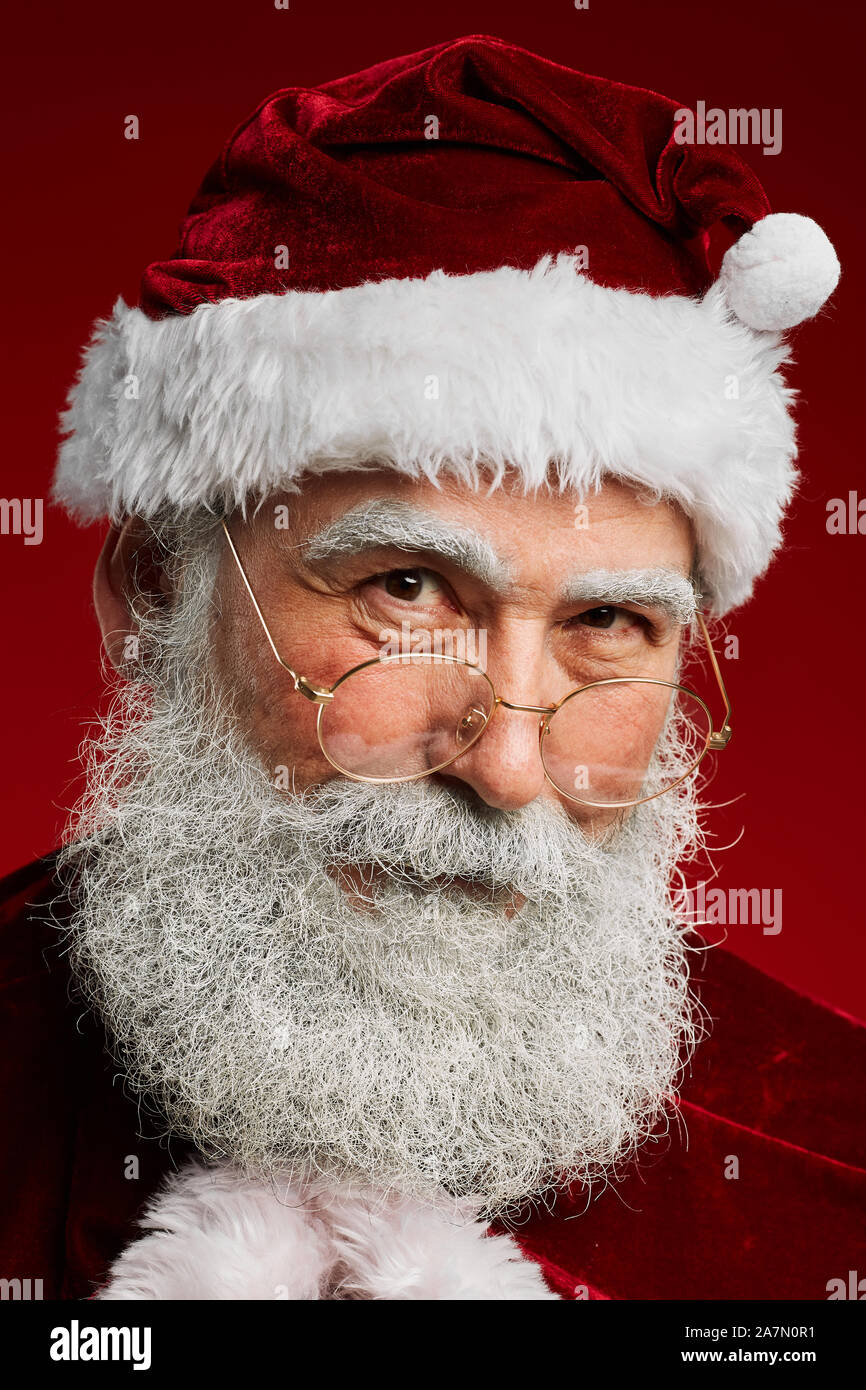 Head and shoulders portrait du père Noël féerique à la caméra à vouloir tout en se posant contre fond rouge Banque D'Images