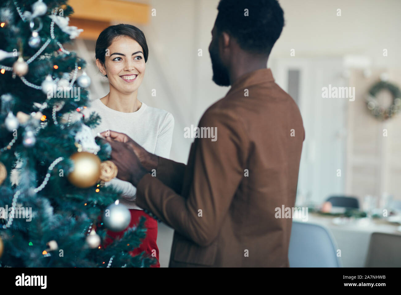 Portrait de race mixte moderne couple decorating Christmas Tree ensemble à la maison, copy space Banque D'Images