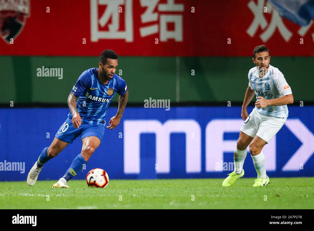 Joueur de football brésilien Alex Teixeira, gauche, de Jiangsu Suning passe le ballon contre un joueur de football israélo-arabe Saba Dia de Guangzhou R&F dans le Banque D'Images