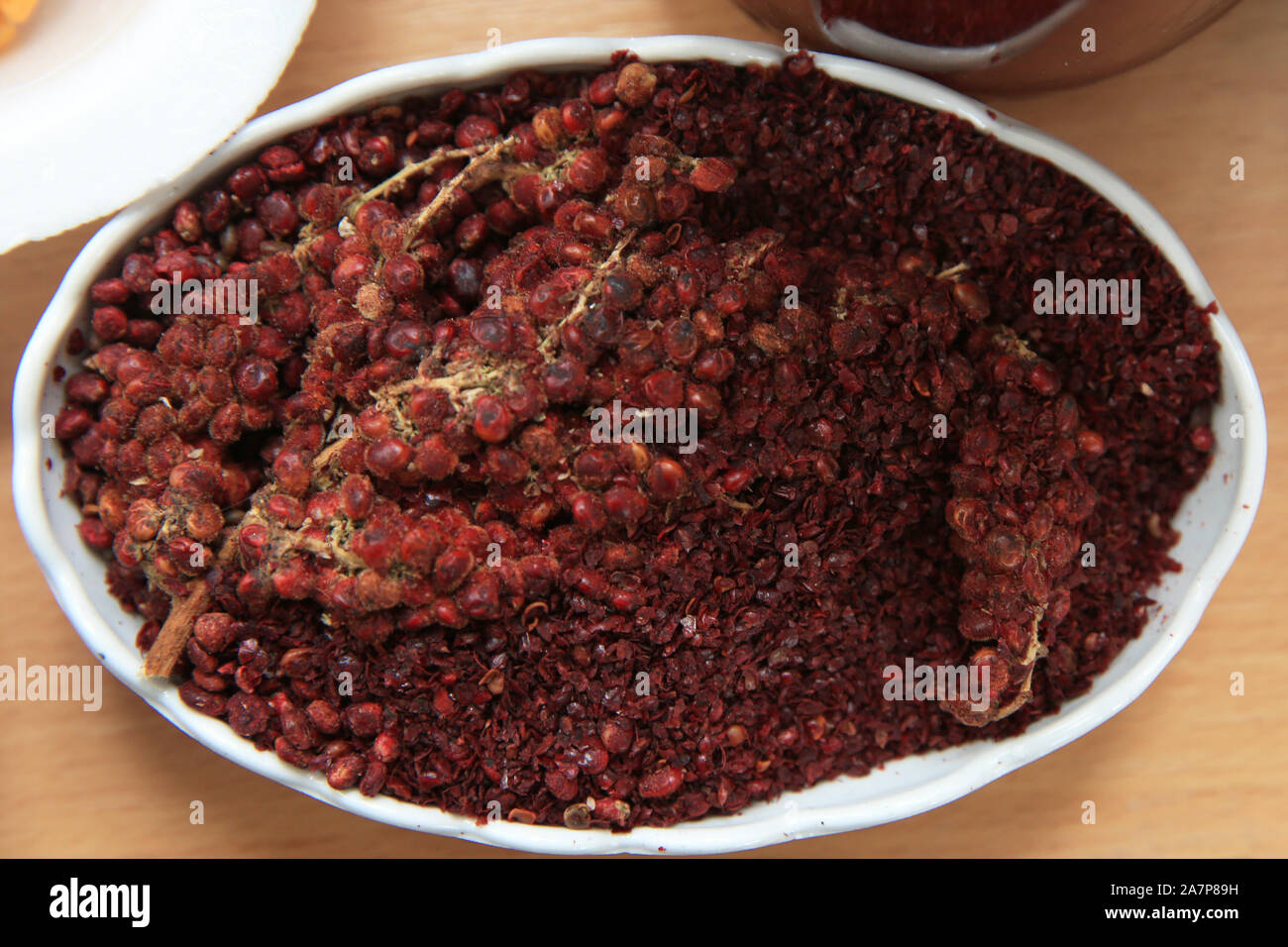 Sumac séchées assaisonnements dans un bol en bois, vue d'en haut. Une poignée de poudre de sumac rouge dans une assiette résumé fond . Sumak céréales et poudre. Le sumac est dans Banque D'Images