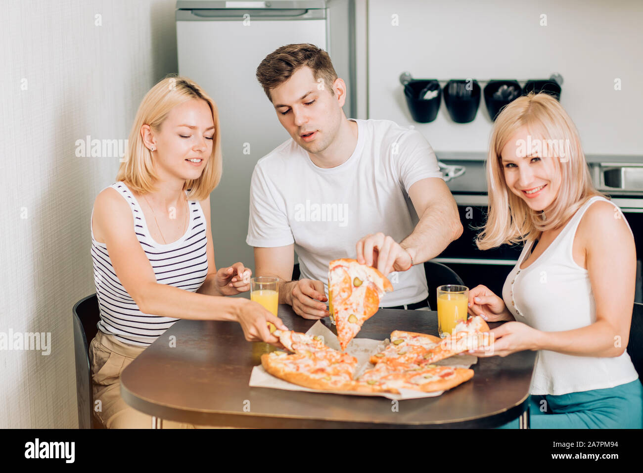 L'amitié, les gens et la société food concept. Trois étudiants heureux caucasienne eating pizza dans la cuisine.Ils ont de la partie à la maison, riant et s'amusant, le dr Banque D'Images