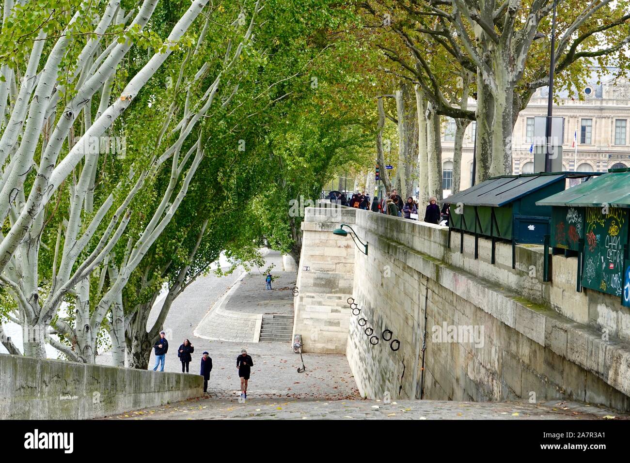 Les gens qui marchent, portant des vêtements d'automne, le long de la partie supérieure et inférieure quai du Louvre le long de la Seine avec boîtes bouquinist vert, Paris, France. Banque D'Images