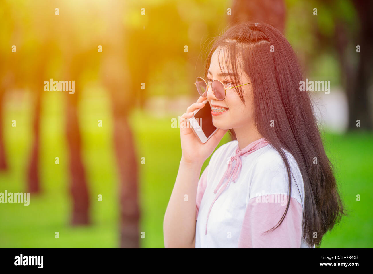 Teen Girl sur smartphone appelant parler sourire heureux extérieure verte nature background. Banque D'Images