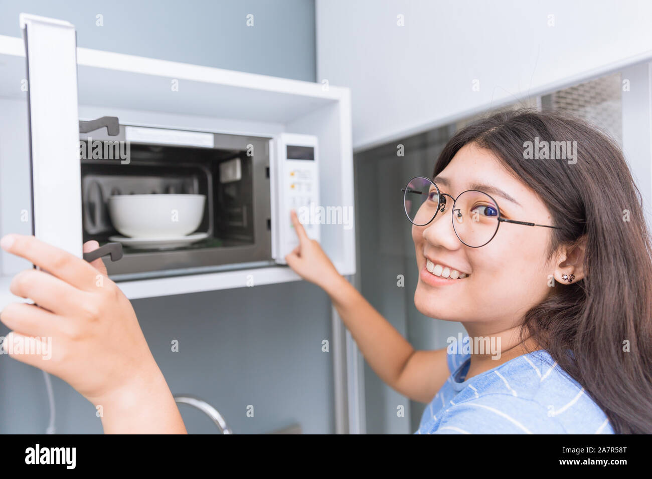 Teen Girl smiling réchauffer des aliments en utilisant des micro-ondes avec bol en céramique en verre. Banque D'Images