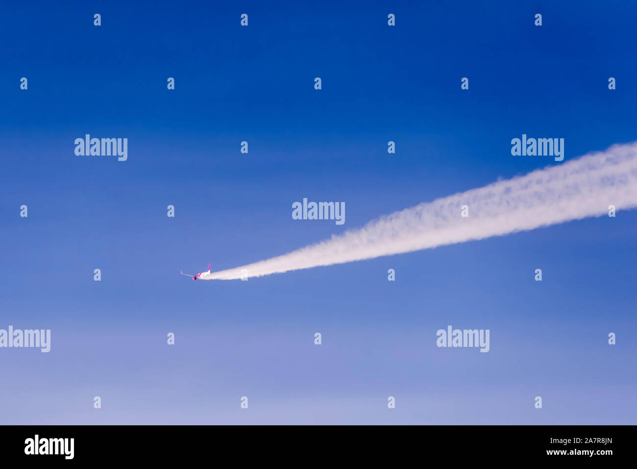 Un avion en vol part une longue piste blanche de fumée derrière elle-même Banque D'Images