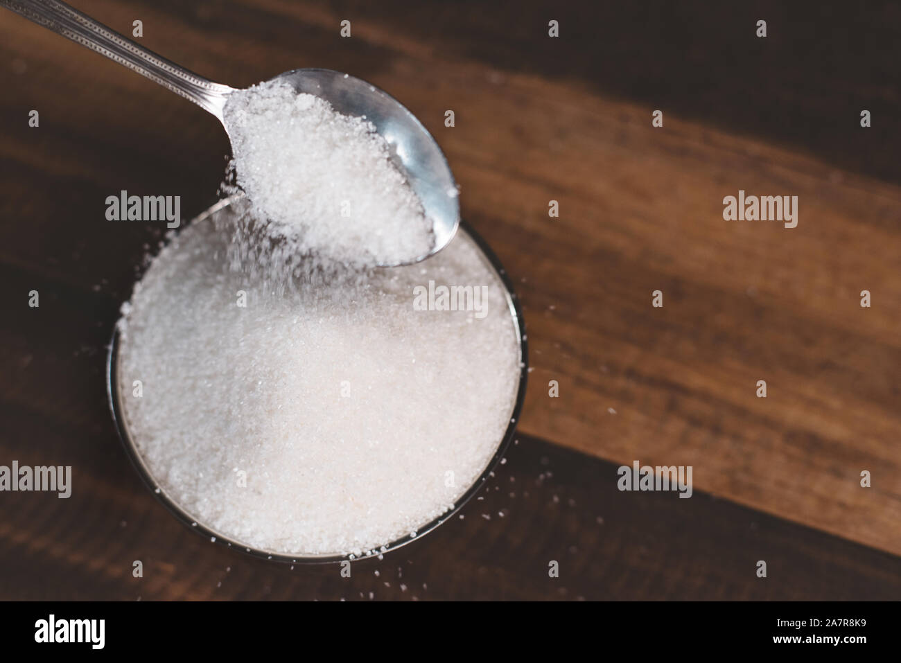 Le sucre versé dans un bol en acier sur une table en bois. Concept de la mauvaise alimentation et le diabète Banque D'Images