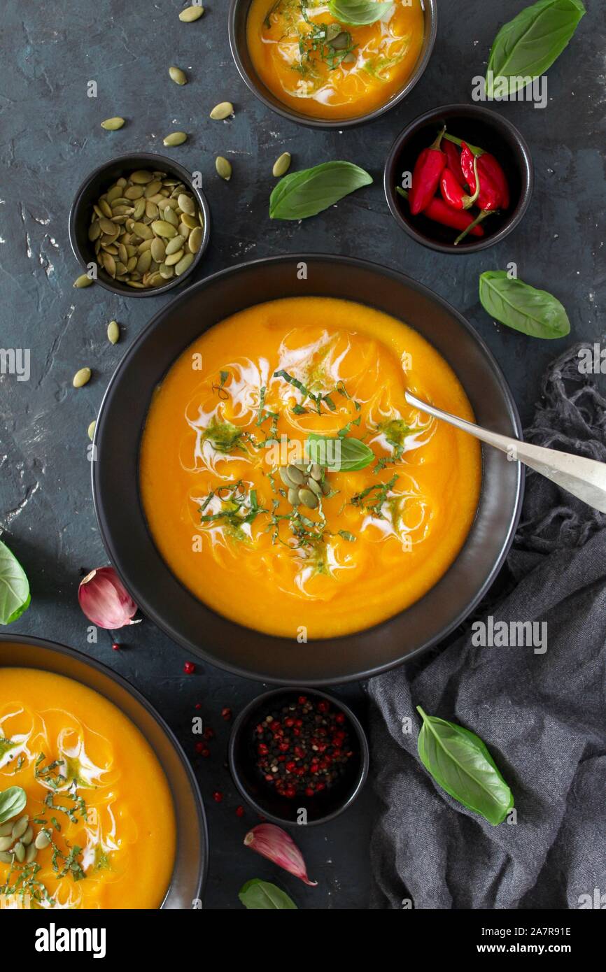 Soupe de carottes et de potiron à la crème et le basilic sur fond sombre. Vue de dessus avec l'exemplaire de l'espace. Banque D'Images