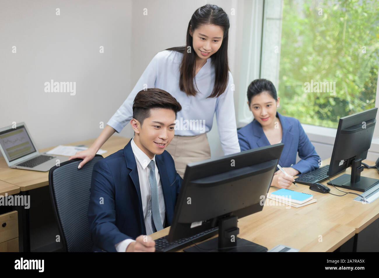 Trois jeune homme et femme d'affaires à la recherche à l'écran d'un ordinateur de l'un d'entre eux tout en travaillant à un bureau dans un bureau Banque D'Images